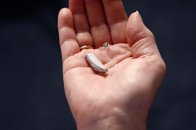 A hand cupped with a digital hearing aid in the palm
